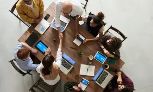 Une équipe diverse se réunit autour d'une table en bois, symbolisant le **travail collaboratif définition**. Ils partagent des idées, des ordinateurs portables et des tablettes, créant une atmosphère dynamique.