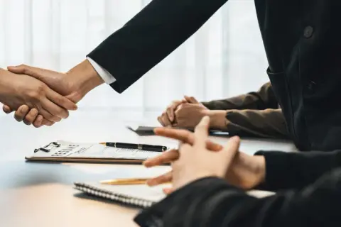 Poignée de main lors d'un entretien d'embauche, avec un CV sur la table. Peut-être discutent-ils d'une clause de sortie conjointe.