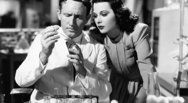 Hedy Lamarr, actrice et inventrice, observe un homme en blouse blanche manipulant des éprouvettes dans un laboratoire.