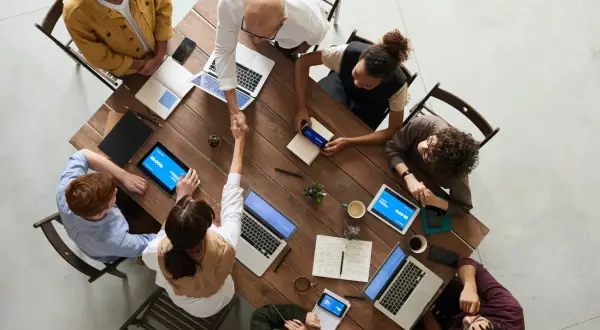 Une équipe diverse se réunit autour d'une table en bois, symbolisant le **travail collaboratif définition**. Ils partagent des idées, des ordinateurs portables et des tablettes, créant une atmosphère dynamique.
