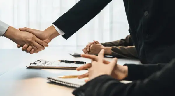 Poignée de main lors d'un entretien d'embauche, avec un CV sur la table. Peut-être discutent-ils d'une clause de sortie conjointe.