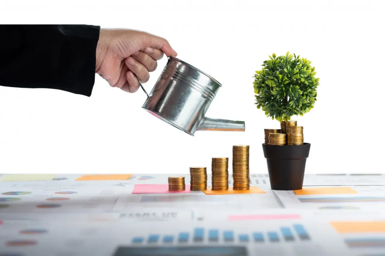 Main qui arrose une plante faite de pièces d'or, symbolisant la croissance d'un nouveau source de revenu.