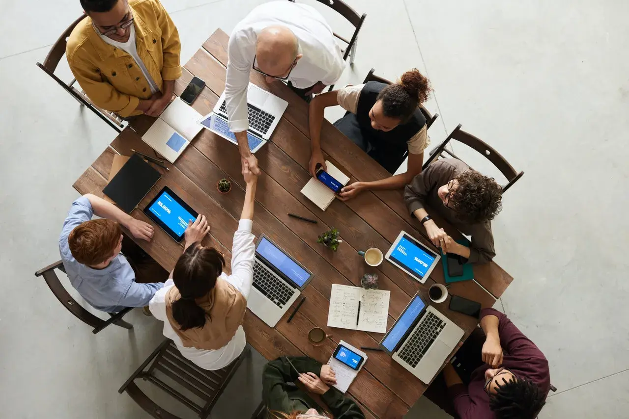 Une équipe diverse se réunit autour d'une table en bois, symbolisant le **travail collaboratif définition**. Ils partagent des idées, des ordinateurs portables et des tablettes, créant une atmosphère dynamique.