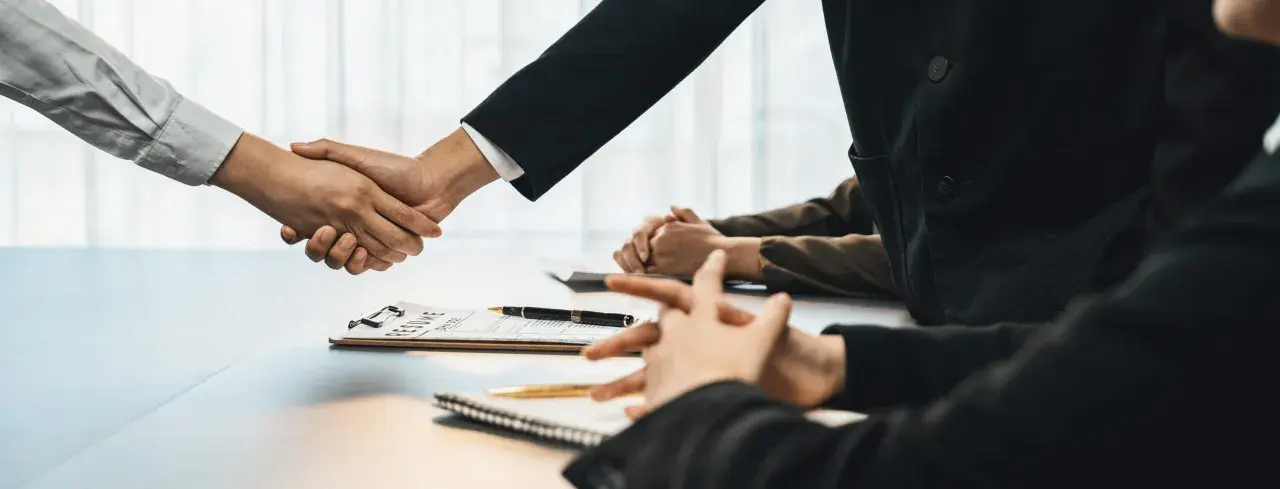 Poignée de main lors d'un entretien d'embauche, avec un CV sur la table. Peut-être discutent-ils d'une clause de sortie conjointe.