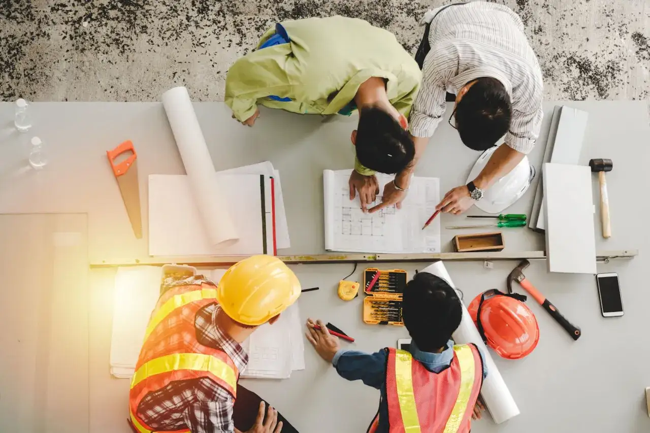 &Eacute;quipe discutant des plans, illustrant la diff&eacute;rence entre ma&icirc;tre d'&oelig;uvre et ma&icirc;tre d'ouvrage. Outils de construction et casques sur la table.