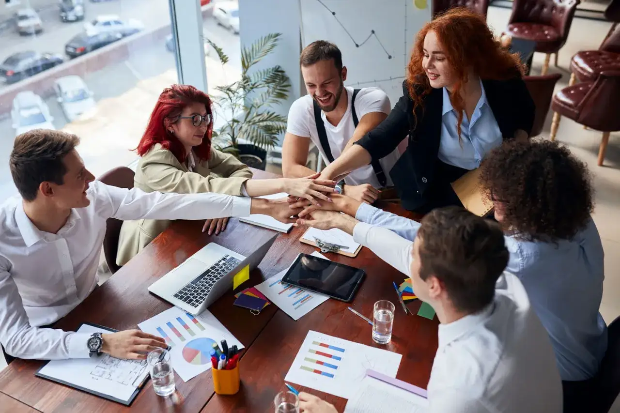 Une &eacute;quipe soud&eacute;e applique une technique de management collaborative, mains jointes au-dessus de la table de r&eacute;union.