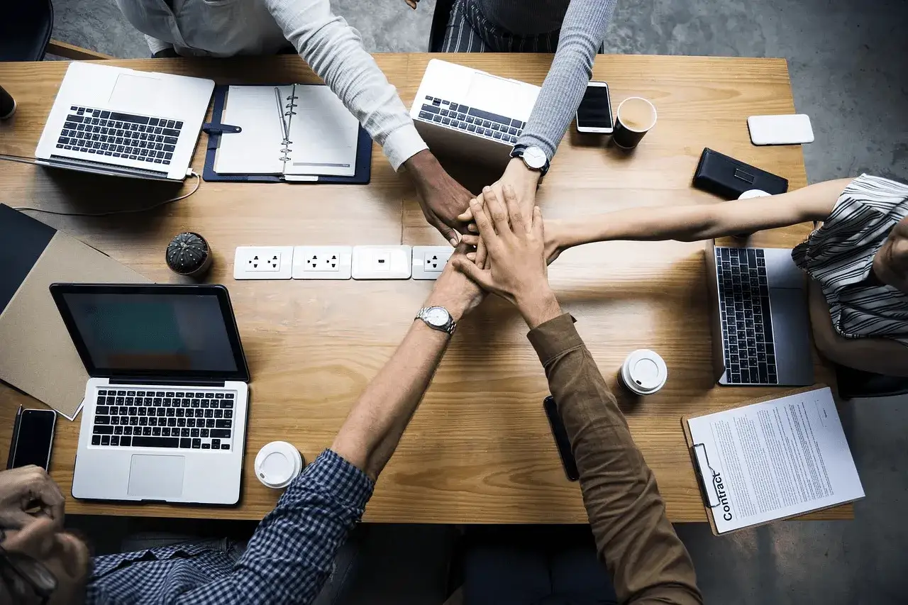 Une &eacute;quipe unie, mains jointes au-dessus d'une table de r&eacute;union, symbolisant la collaboration pour une etude de cas gestion de projet r&eacute;ussie.
