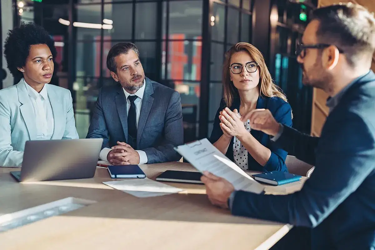 Des hommes et femmes d'affaires discutent autour d'une table, le contrat en main, démontrant leur pouvoir de négociation.