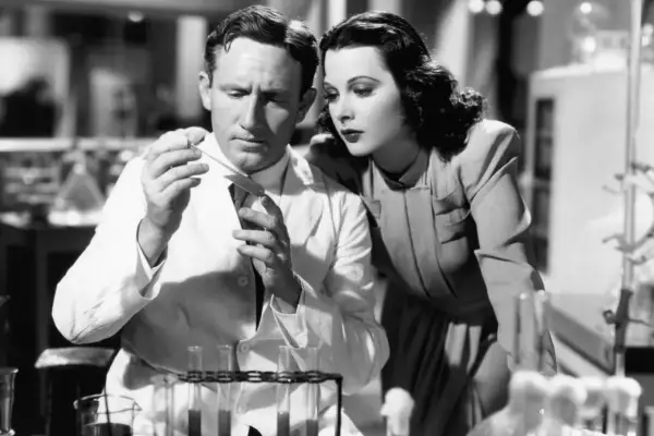 Hedy Lamarr, actrice et inventrice, observe un homme en blouse blanche manipulant des éprouvettes dans un laboratoire.