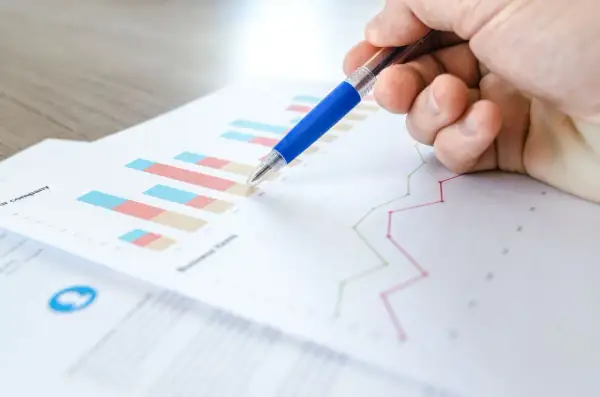 Main d'une personne pointant un graphique avec un stylo bleu. L'image illustre la veille informationnelle def.